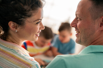 Caucasian parents share an affectionate moment in casual attire at home, while their school-aged...