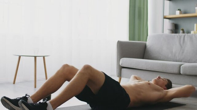 A sporty young man performs exercises on a mat in his living room, focusing on fitness and well-being. His dedication to a healthy lifestyle is evident in his workout routine.