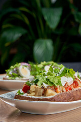 A vibrant and colorful spread of two smorrebrod, traditional Danish open-faced sandwiches, topped with fresh vegetables, herbs, and creamy spreads.