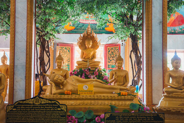 Serene temple interior in Thailand featuring a reclining Buddha, seated Buddhas, vibrant murals, floral decorations, and ornate red and gold doors.