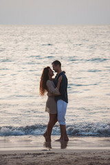 A couple stands on a serene beach in Thailand, embracing near gentle waves under soft light. Their...