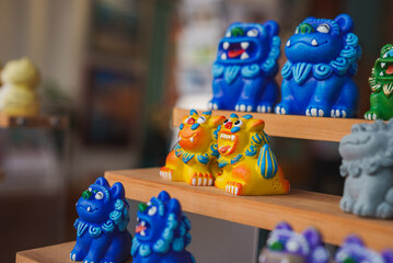 Vibrant blue and yellow ceramic lion figurines with intricate details displayed on wooden shelves in an indoor setting, likely a shop or market in Thailand.