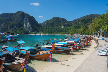 Turquoise waters, limestone cliffs, and lush green hills frame a sandy beach with long tail boats...