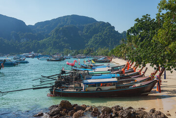 A serene beach on Koh Phi Phi islands, Thailand, with long tail boats on the shore, turquoise...