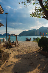 Golden sand meets turquoise waters in Koh Phi Phi, Thailand, with long tail boats, limestone cliffs, a wooden swing, and tropical plants in view.