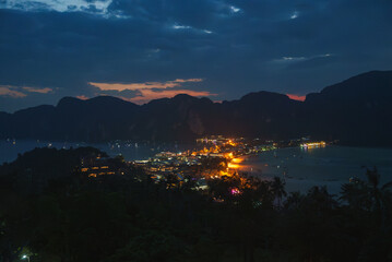 Koh Phi Phi's vibrant lights reflect on the water, surrounded by dark limestone cliffs and lush...