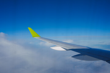 View of an airplane wing featuring a bright green wingtip, captured mid flight with a clear blue sky and scattered clouds visible below.