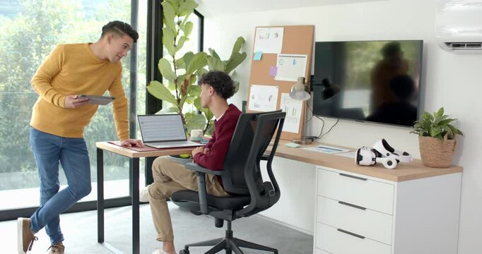 Discussing work, multiracial gay couple using laptop and tablet in modern home office - Powered by Adobe