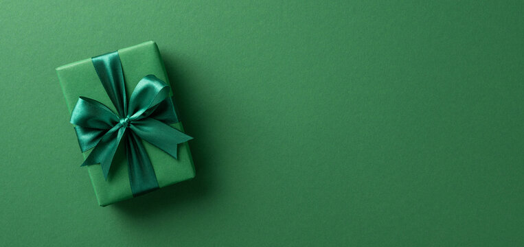 An elegant green gift box wrapped with satin ribbon, placed on a matching green background, perfect for celebrations and festive occasions