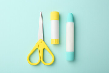 Glue and scissors on turquoise background, flat lay