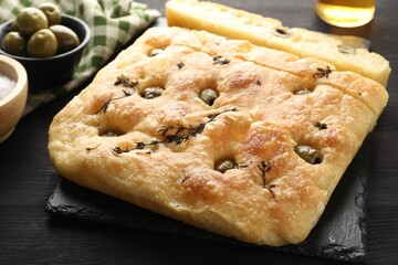 Pieces of delicious focaccia bread with olives and thyme on dark wooden table, closeup