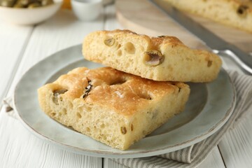 Pieces of delicious focaccia bread with olives, thyme and salt on white wooden table, closeup