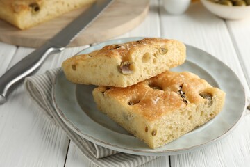 Pieces of delicious focaccia bread with olives, thyme, salt and knife on white wooden table, closeup