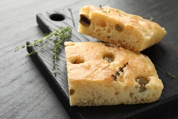 Pieces of delicious focaccia bread with olives and thyme on black table, closeup