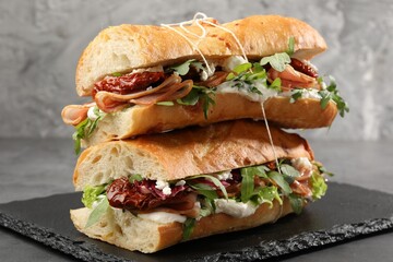 Halves of baguette sandwich with prosciutto and sun dried tomatoes on grey table, closeup