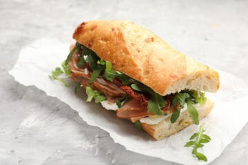 Baguette sandwich with ham and sun dried tomatoes on grey textured table, closeup