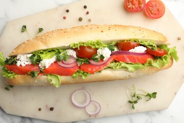 Delicious baguette with salmon on white marble table, top view