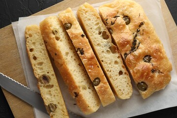 Slices of delicious focaccia bread with olives, thyme, salt and knife on black table, top view