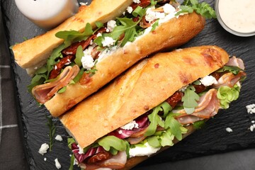 Halves of baguette sandwich with prosciutto and sun dried tomatoes and ingredients on grey table,...
