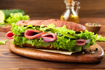 Delicious baguette sandwich with ham on wooden table, closeup