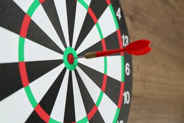 Dart board and red arrow on wooden background, closeup