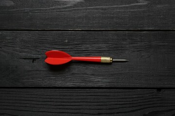 One red dart arrow on black wooden table, top view