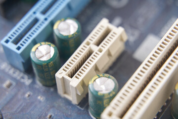 Close up of computer motherboard with capacitors and pci slots in focus.