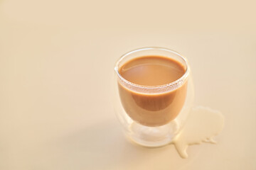 Double walled glass cup with spilled coffee on light beige surface.