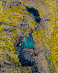 Aerial view of turquoise ponds in a mossy canyon, South Iceland's rugged terrain.