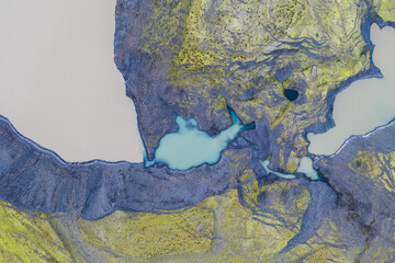 Aerial view of turquoise ponds in a mossy canyon, South Iceland's rugged terrain.