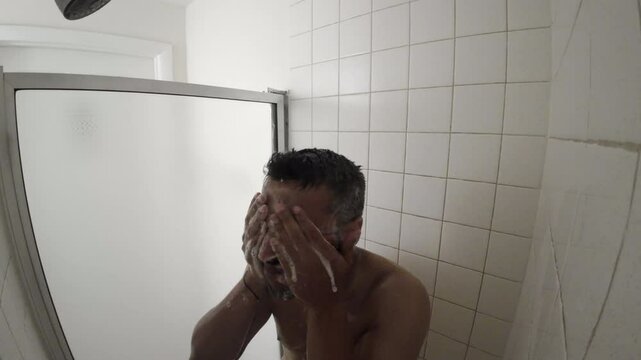 A man is in the shower with his hands on his head. He is smiling and he is enjoying himself