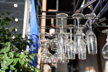Empty wine glasses hanging upside down at a bar with sunlight and greenery in background.