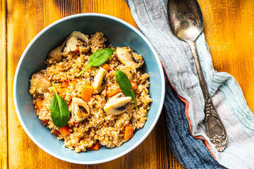 Boiled spelled or spelled porridge with mushrooms, carrots and spinach in a blue bowl on a wooden background with a napkin and spoon. Healthy eating concept. Vegetarian dish.