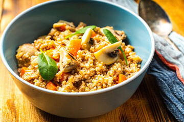 Boiled spelled or spelled porridge with mushrooms, carrots and spinach in a blue bowl on a wooden background with a napkin and spoon. Healthy eating concept. Vegetarian dish.