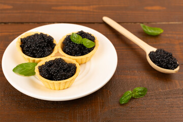 Tartlets with black caviar served on on wooden table