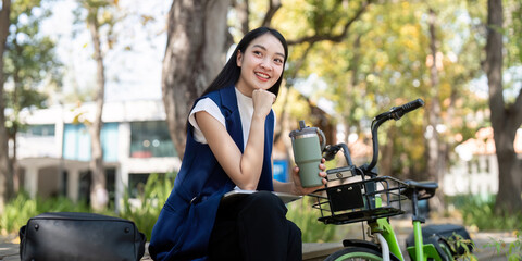 Friendly businesswoman enjoying a refreshing drink while seated beside her green bicycle in an eco friendly park