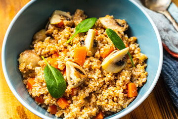 Boiled spelled or spelled porridge with mushrooms, carrots and spinach in a blue bowl on a wooden background with a napkin and spoon. Healthy eating concept. Vegetarian dish.