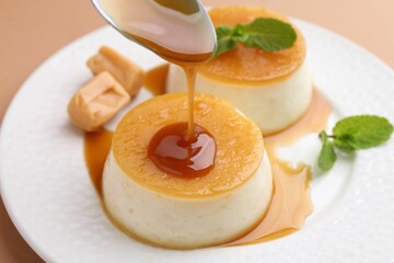 Pouring caramel sauce onto tasty pudding on light brown background, closeup