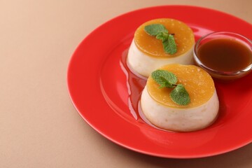 Tasty puddings with caramel sauce served on light brown background, closeup. Space for text