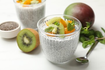 Delicious chia pudding with fruits in glasses, mint and spoon on white table, closeup