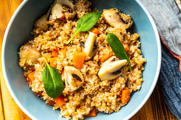 Boiled spelled or spelled porridge with mushrooms, carrots and spinach in a blue bowl on a wooden background with a napkin and spoon. Healthy eating concept. Vegetarian dish.