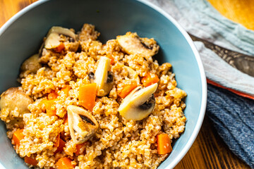 Boiled spelled or spelled porridge with mushrooms, carrots and spinach in a blue bowl on a wooden background with a napkin and spoon. Healthy eating concept. Vegetarian dish.