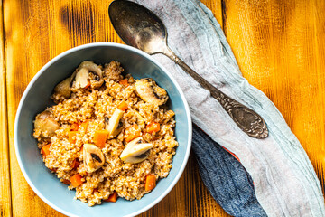 Boiled spelled or spelled porridge with mushrooms, carrots and spinach in a blue bowl on a wooden background with a napkin and spoon. Healthy eating concept. Vegetarian dish. Copyspace