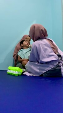 A child with cerebral palsy accompanied by his mother is undergoing oral stimulation using a special needs brush assisted by a speech therapist in the children's medical rehabilitation room.