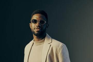 Stylish young man wearing sunglasses and a beige coat, exuding confidence against a dark gradient background with a modern aesthetic