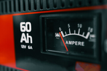 Close-up view of a battery charger with an ampere gauge and capacity indicator displaying 60 Ah. The red needle points to full charge on a black and red device