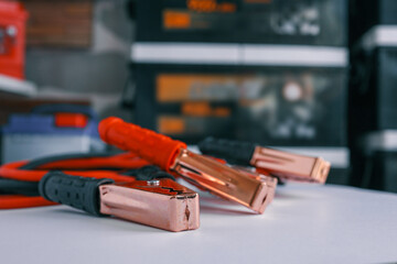 Close-up of copper battery jumper clamps with red and black insulated handles. Background shows...