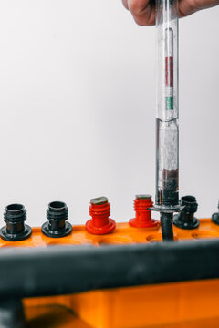 A close-up of a hydrometer measuring fluid density in a yellow car battery. Visible red and black terminals highlight battery components