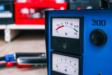 Close-up of a blue charging station featuring analog voltage and amperage meters with calibration...