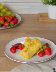 Yellow bright pancakes with fresh strawberries on a white plate stands on the table
